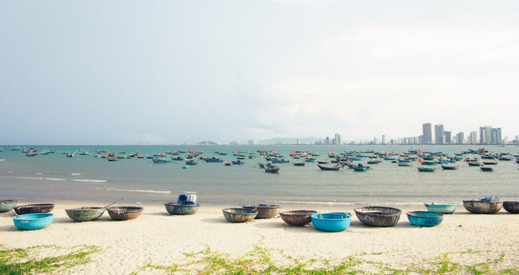 Boats line the ocean shore near a city skyline.-An Binh Island Vietnam