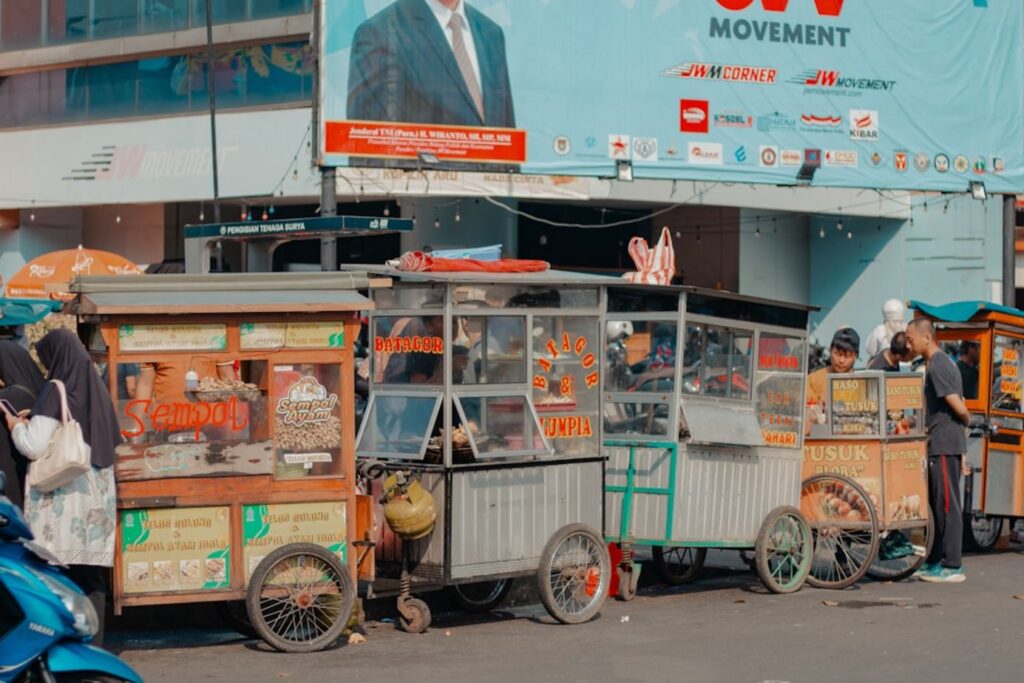 Street food carts are parked along a busy road.-Lembata Indonesia
