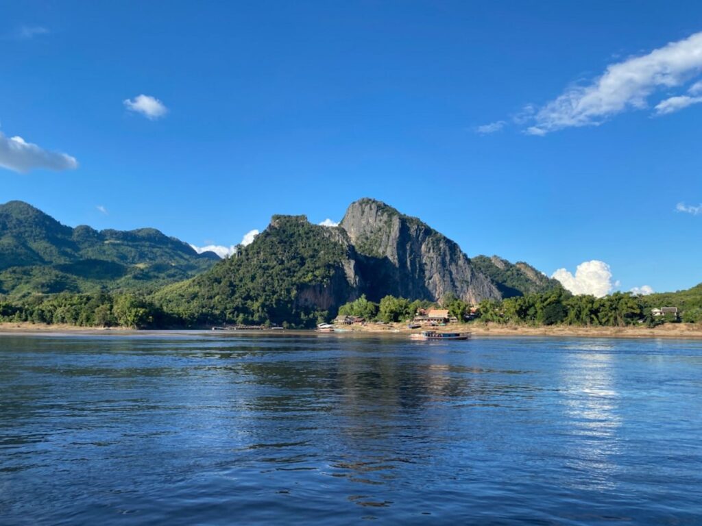 Mountain overlooks a serene river under a bright blue sky.-laos money
