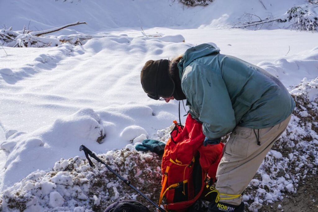 Person in winter gear packing red backpack in snow.-Kuwait packing