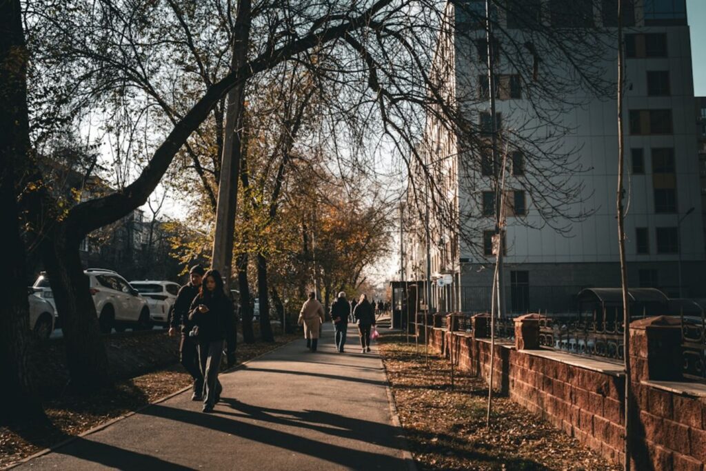 People walking on a sunny sidewalk next to buildings.-Kazakhstan