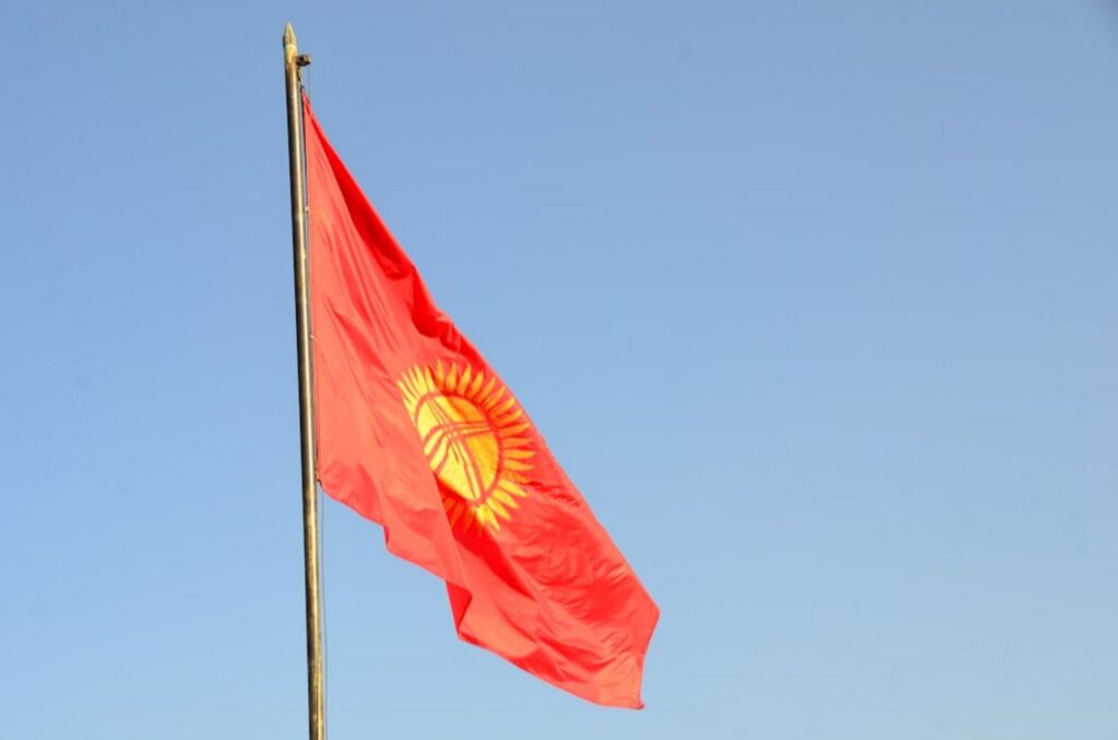 Red flag with sun symbol against clear blue sky-Kyrgyzstan flights