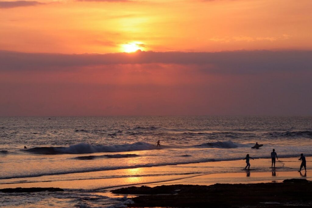 A group of people standing on top of a beach next to the ocean-canggu Indonesia