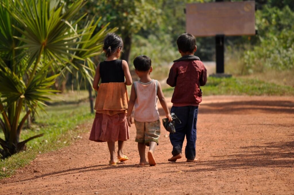 Kledingadvies voor Cambodja: comfortabel en respectvol reizen 1 Three children walk along a dirt path.-Cambodjakleding