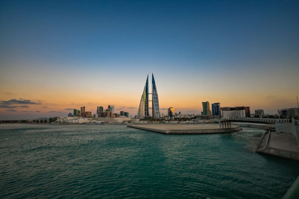 Modern buildings silhouetted at sunset over water.-saar Bahrain